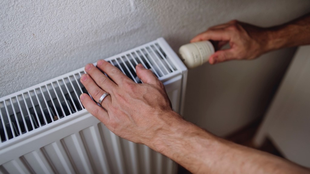 Jemand schaltet eine Heizung ein und kontrolliert die Temperatur mit der Hand.