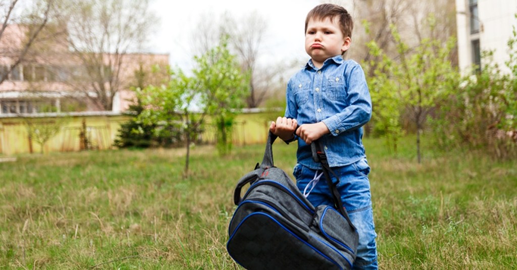 Junge versucht schweren Schulranzen anzuheben