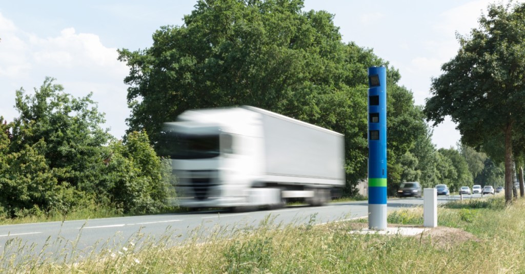 ein weißer Lkw fährt an einer blauen Säule am Straßenrand vorbei