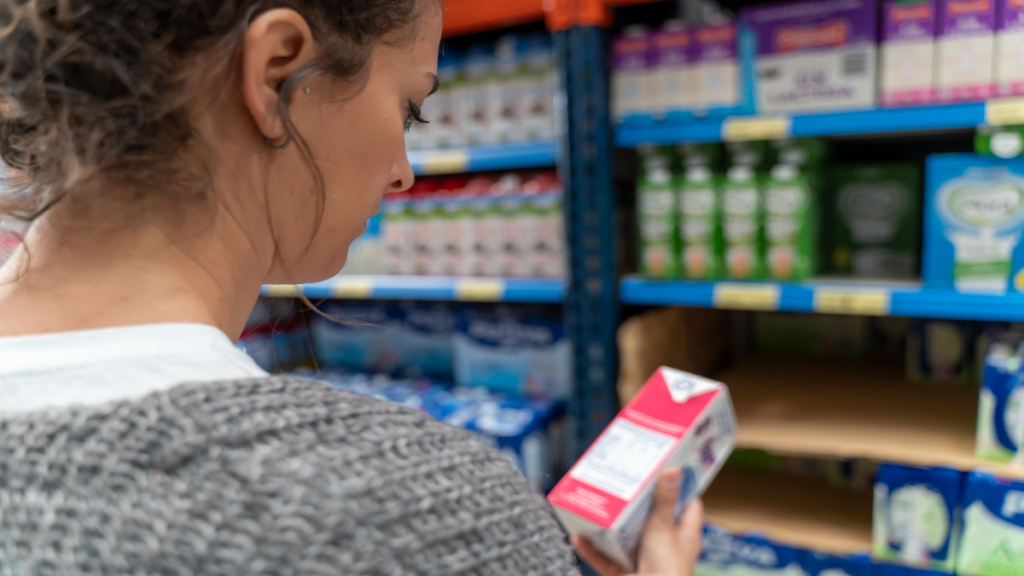 Frau schaut auf eine Tüte Milch im Supermarkt.