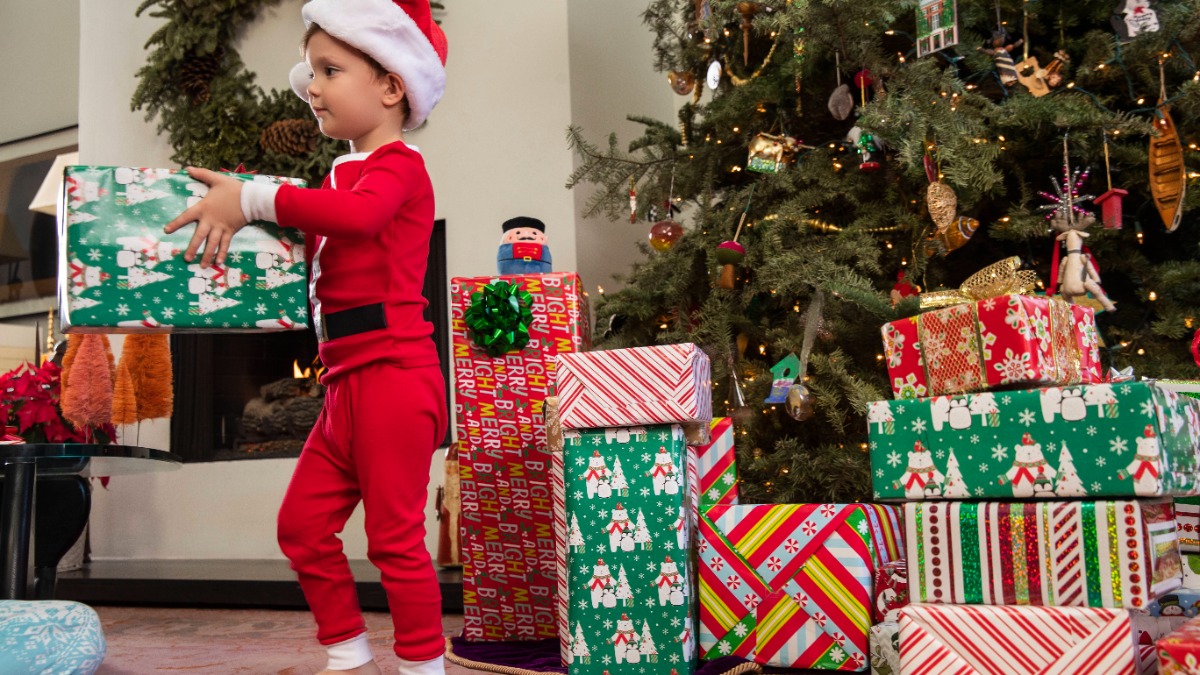 kleiner Junge im WeihnachtskostÃ¼m und ein Weihnachtsbaum, unter dem viele Geschenke liegen