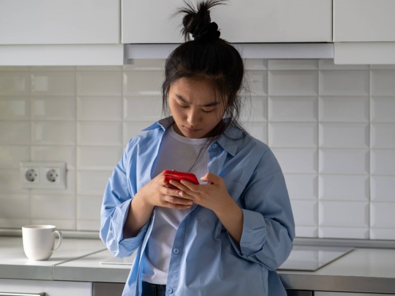 eine junge Frau steht in der KÃ¼che und tippt in ihr Telefon