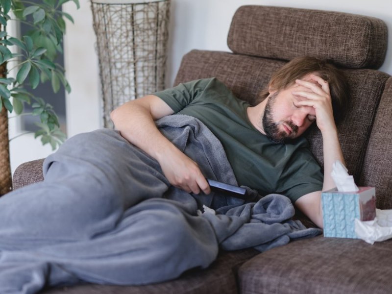 Ein Mann liegt auf dem Sofa und hält sich seinen schmerzenden Kopf.