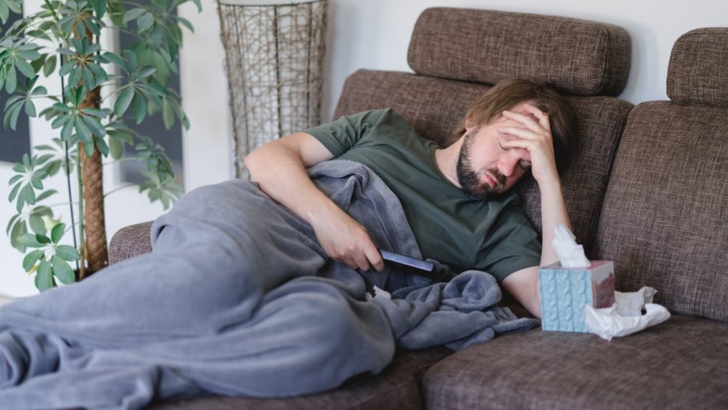 Ein Mann liegt auf dem Sofa und hält sich seinen schmerzenden Kopf.