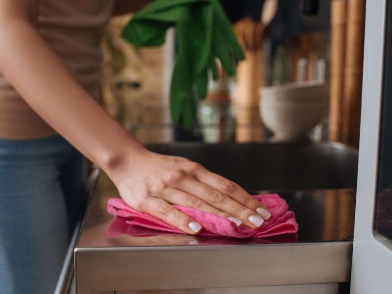 eine Frau wischt eine Küchenarbeitsplatte mit einem Tuch ab