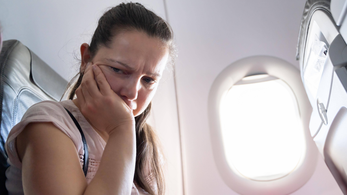 Frau mit Flugangst sitzt im Flugzeug und hat den Kopf auf die Hand gestützt.