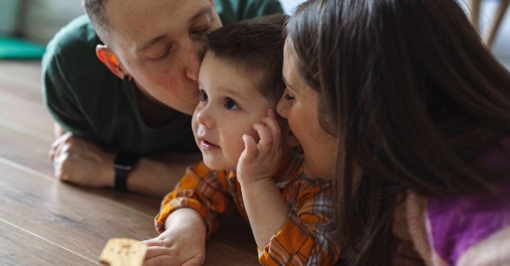 Vater und Mutter küssen ihren Sohn, alle liegen auf dem Boden