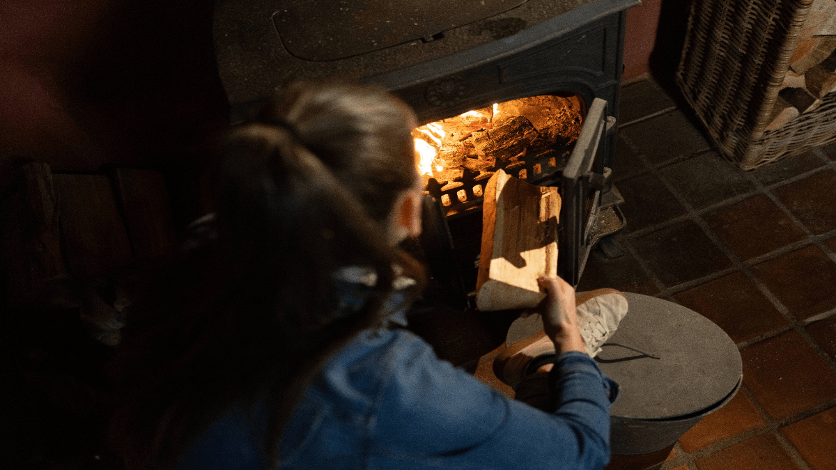 Eine Frau legt einen Holzscheit in einen Kamin.