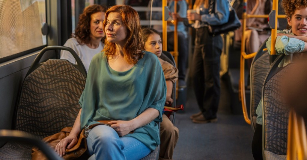 Passagiere in einem Bus, der Fokus liegt auf einer Frau, deren Platz neben ihr frei ist