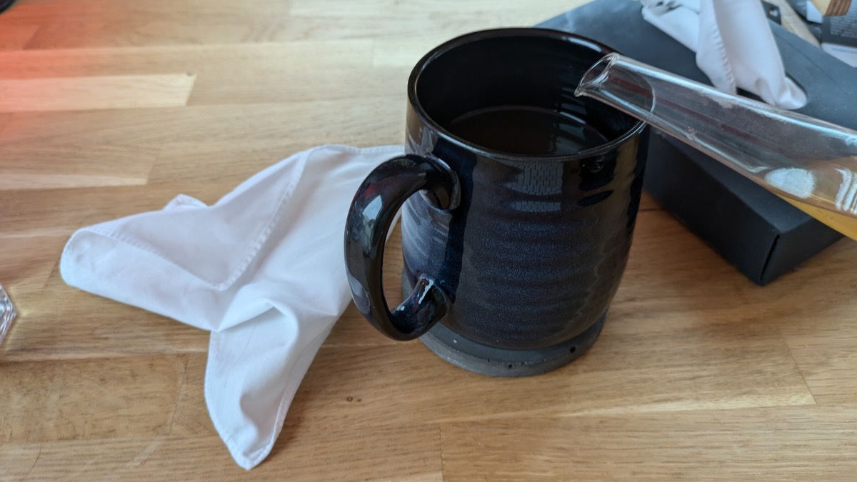 Eine blaue Teetasse, in die Tee eingegossen wird. Daneben liegt ein zerknÃ¼lltes Taschentuch.