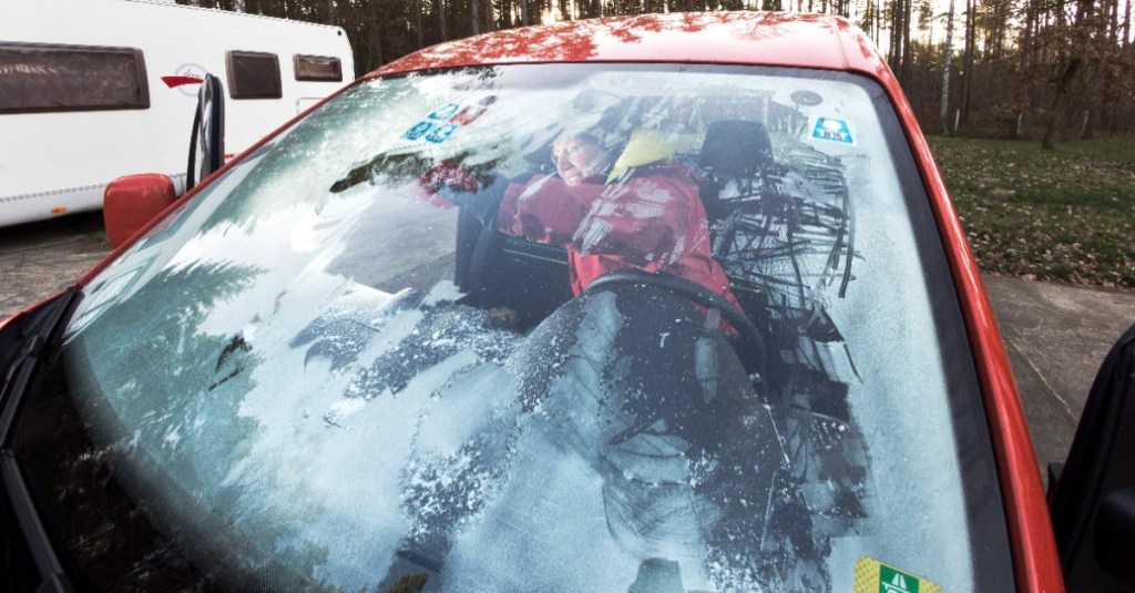 eine Frau kratzt ihre vereiste Autoscheibe von innen frei