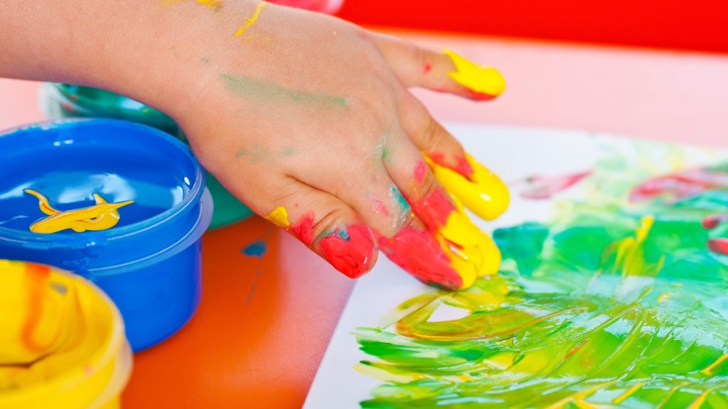 Eine Hand, die mit den Fingern Farbe auf ein Papier aufmalt.