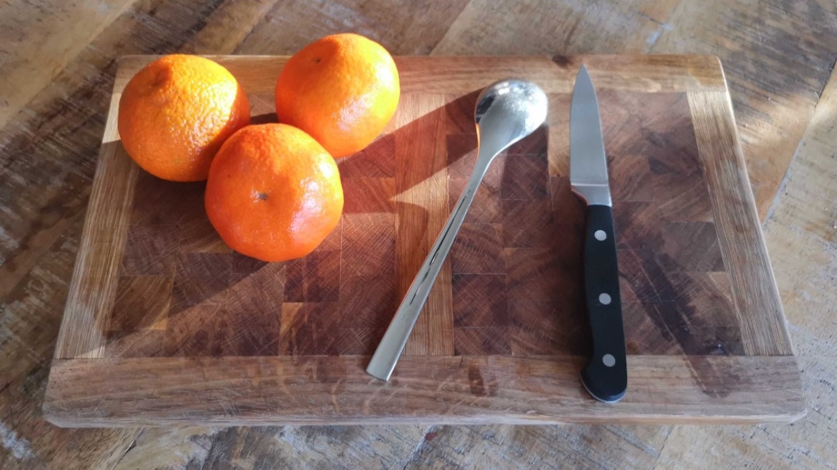 Mandarinen schÃ¤len: drei Mandarinen, ein EsslÃ¶ffel und ein Messer liegen auf einem Holzbrett