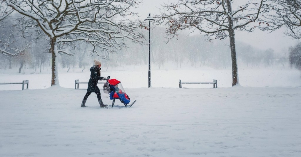 Weihnachten feiern: Frau geht im Schnee mit einem Kinderwagen spazieren