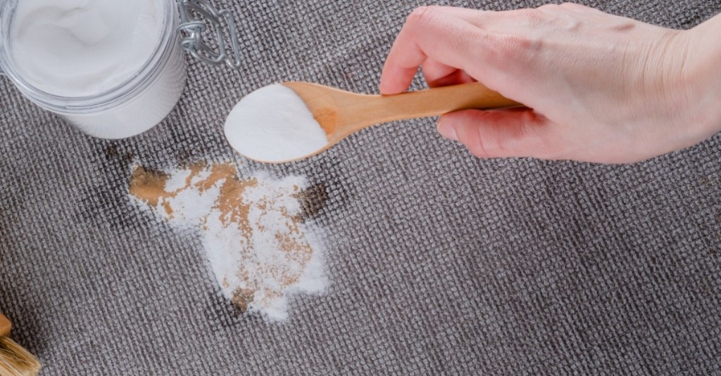 Erbrochenes aus Teppich entfernen: jemand schüttet ein weißes Pulver auf einen Fleck im Teppich