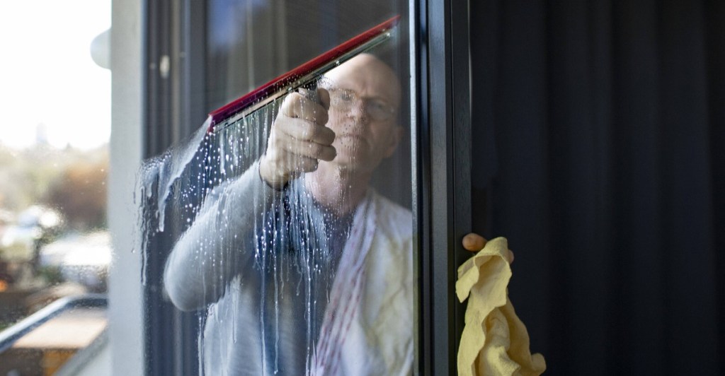 Mieter Fenster putzen: Mann beim Fensterputzen mit einer Gummiflitsche