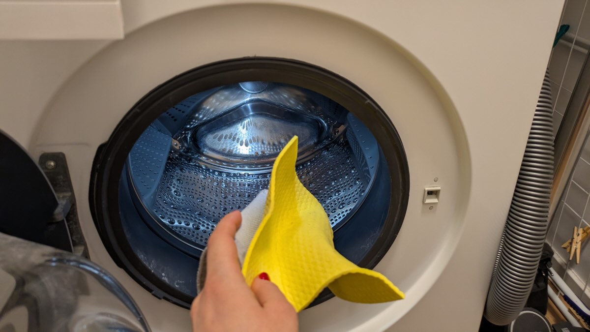 Eine Person steckt einen gelben Putzlappen in die WÃ¤schetrommel einer Waschmaschine.