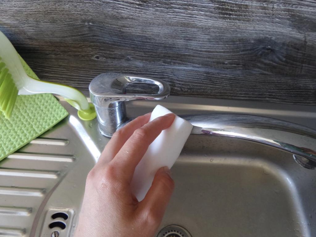 Kalkflecken auf einem Wasserhahn werden mit einem Schmutzradierer behandelt.