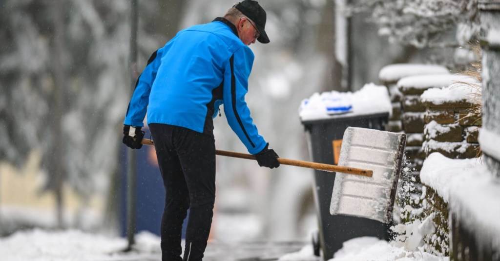 Schnee räumen: ein älterer Herr schippt Schnee auf dem Gehweg