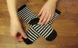 Hände werden von oben fotografiert, wie sie Socken zusammenlegen.
