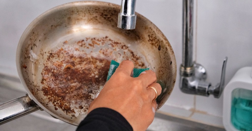 Aluminium reinigen: eine verdreckte Pfanne wird mit einem Schwamm gereinigt