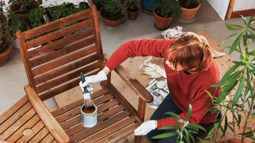 Eine Frau ölt einen Gartenstuhl aus Holz.