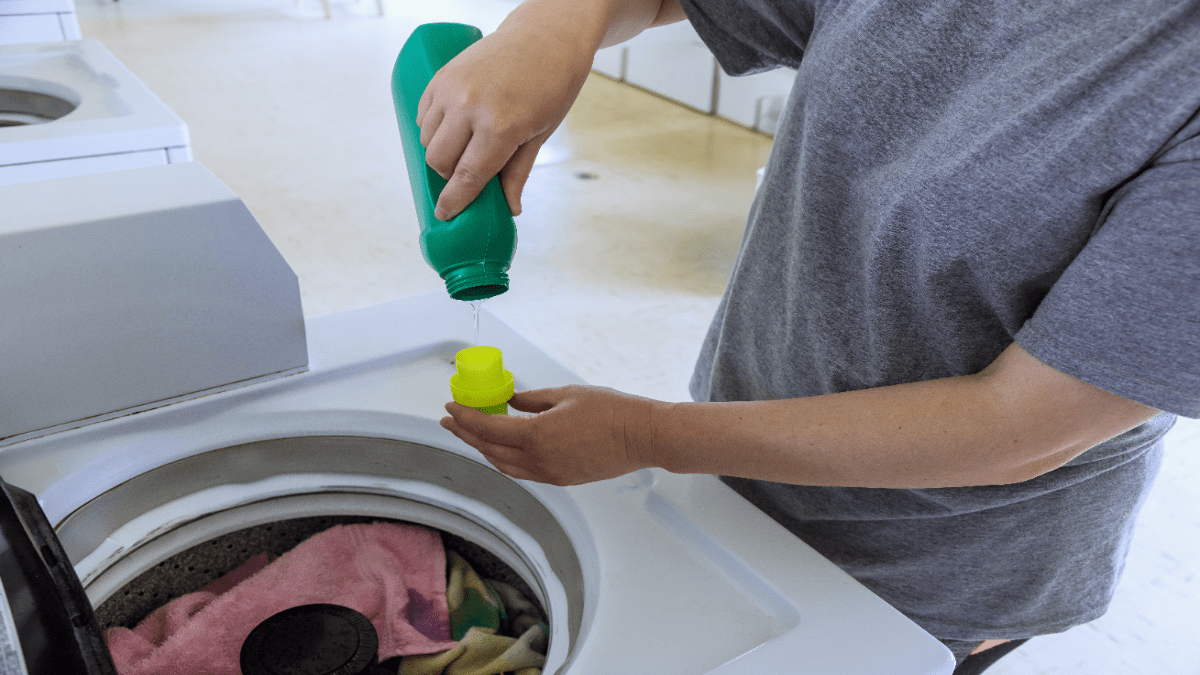 Eine Person schüttet Hygienespüler in eine Wäschetrommel.