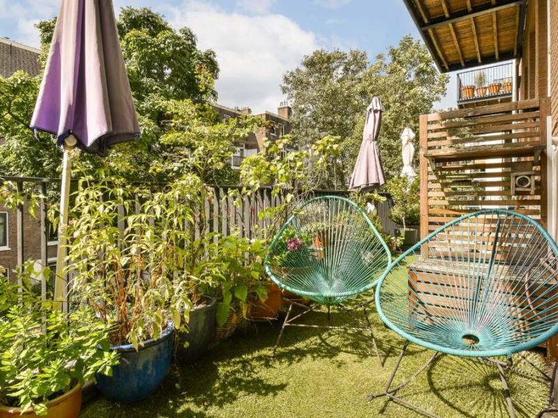 Ein Balkon, gestaltet mit Korbstühlen, Kunstrasen, Pflanzen und Sichtschutz.