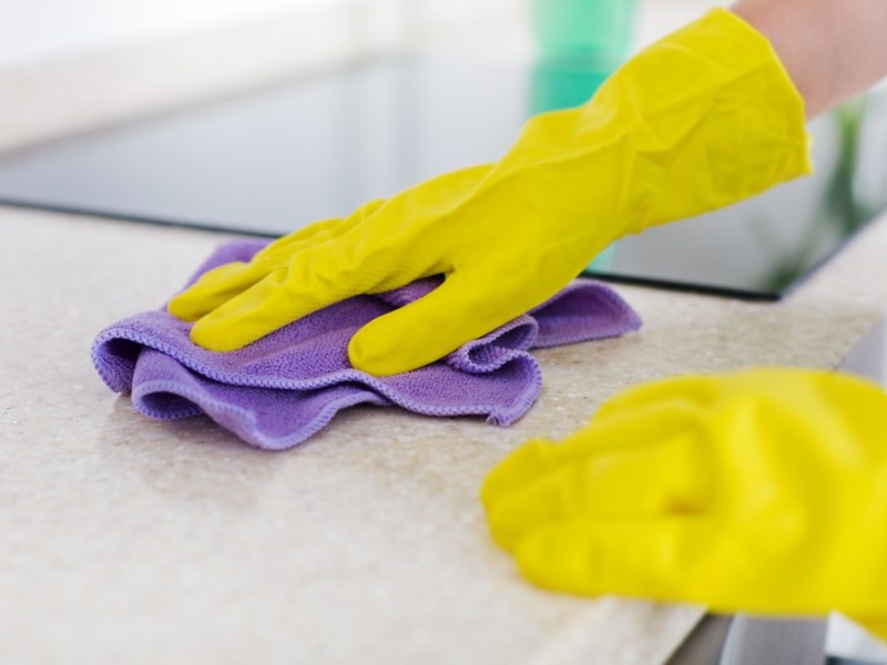 eine Frau mit gelben Putzhandschuhen reinigt eine Küchenarbeitsplatte mit einem lila Schwammtuch