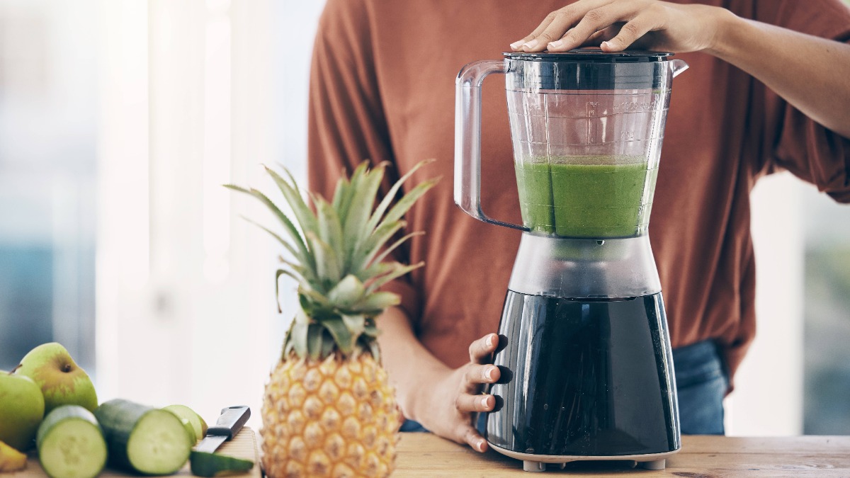 eine Frau bereitet sich einen grünen Smoothie in einem Standmixer zu