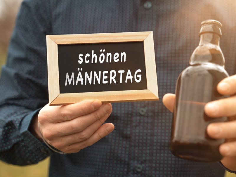 Mann mit Bier und einem Schild, auf dem steht: „Schönen Männertag“.
