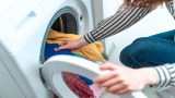 Eine Person steckt Buntwäsche in eine Waschmaschine.