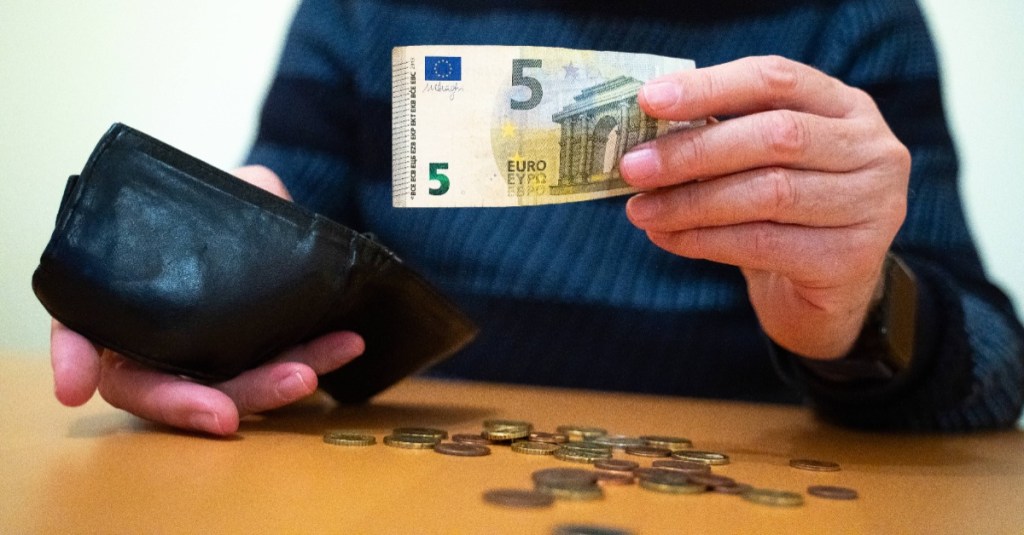 Ein Rentner hält einen 5-Euro-Schein in der Hand, während sein Portemonnaie fast leer ist