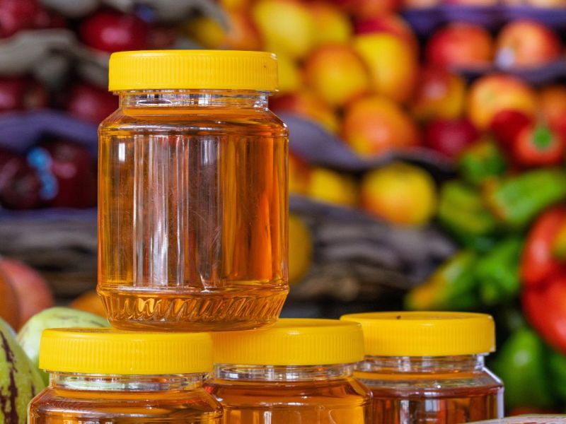 Ein Glas Honig vor einem Regal voller frischem Obst