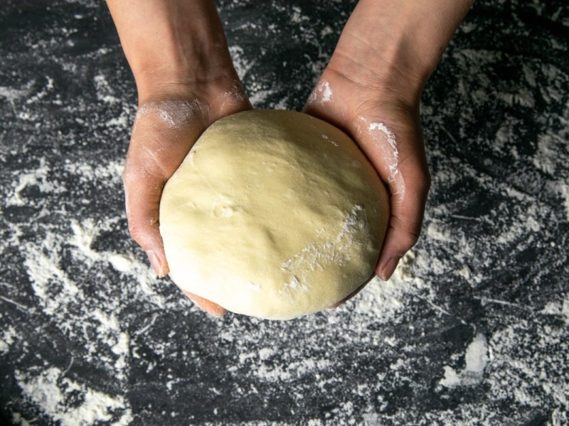 Pizzateig wird zu einer Kugel geformt in zwei Händen gehalten.