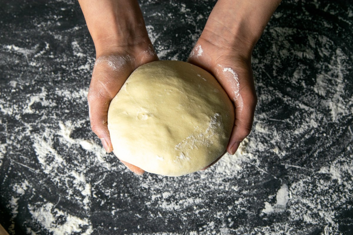 Pizzateig wird zu einer Kugel geformt in zwei Händen gehalten.