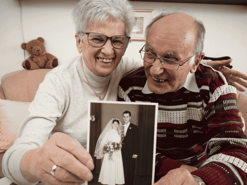 Hochzeitstage Namen, Älteres Ehepaar hält Hochzeitsfoto in die Kamera