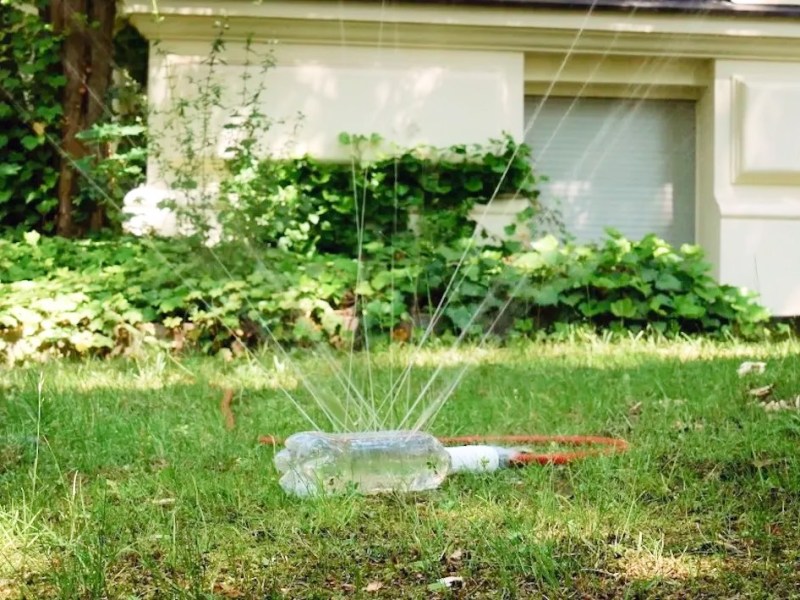 Ein selbst gebauter Rasensprenger aus einer Plastikflasche bewässert einen Rasen in einem Garten.