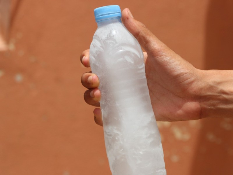 eine Hand hält eine Plastikflasche mit gefrorenem Wasser