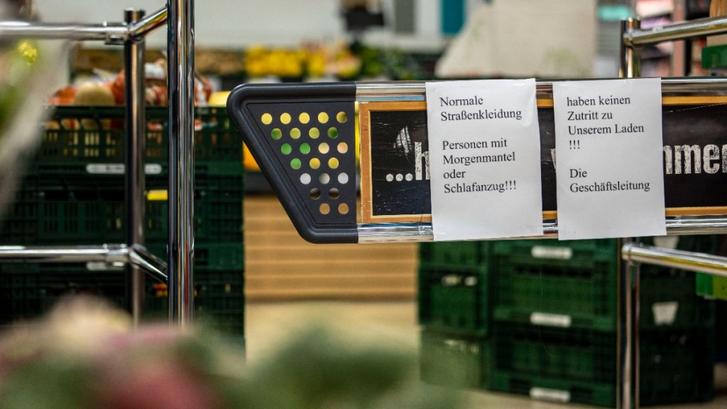 an einem Eingang zum Supermarkt hängen Schilder, dass Personen mit Bademantel nicht hineindürfen