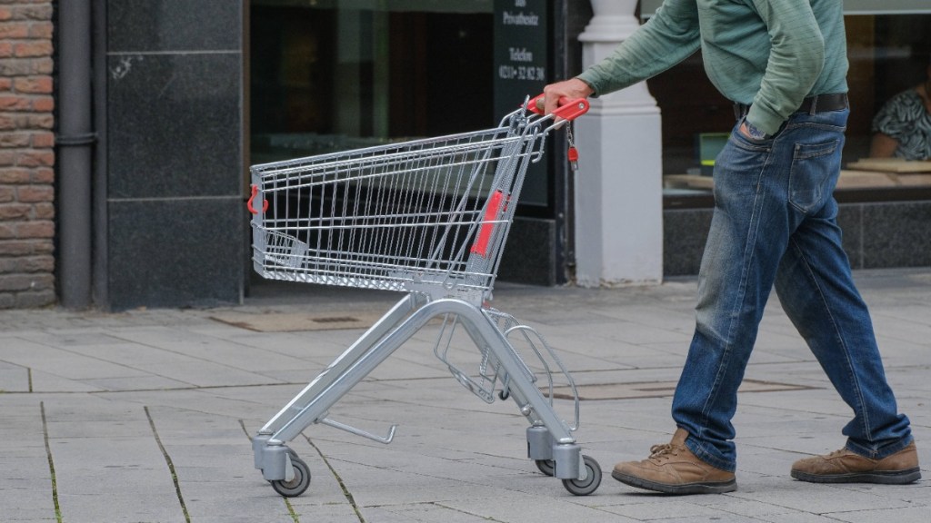 ein Mann schiebt einen leeren Einkaufswagen über die Straße
