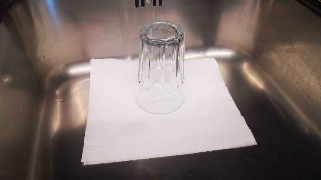 in einer Spüle wird der Abfluss durch ein Küchentuch abgedeckt, darauf steht ein Glas